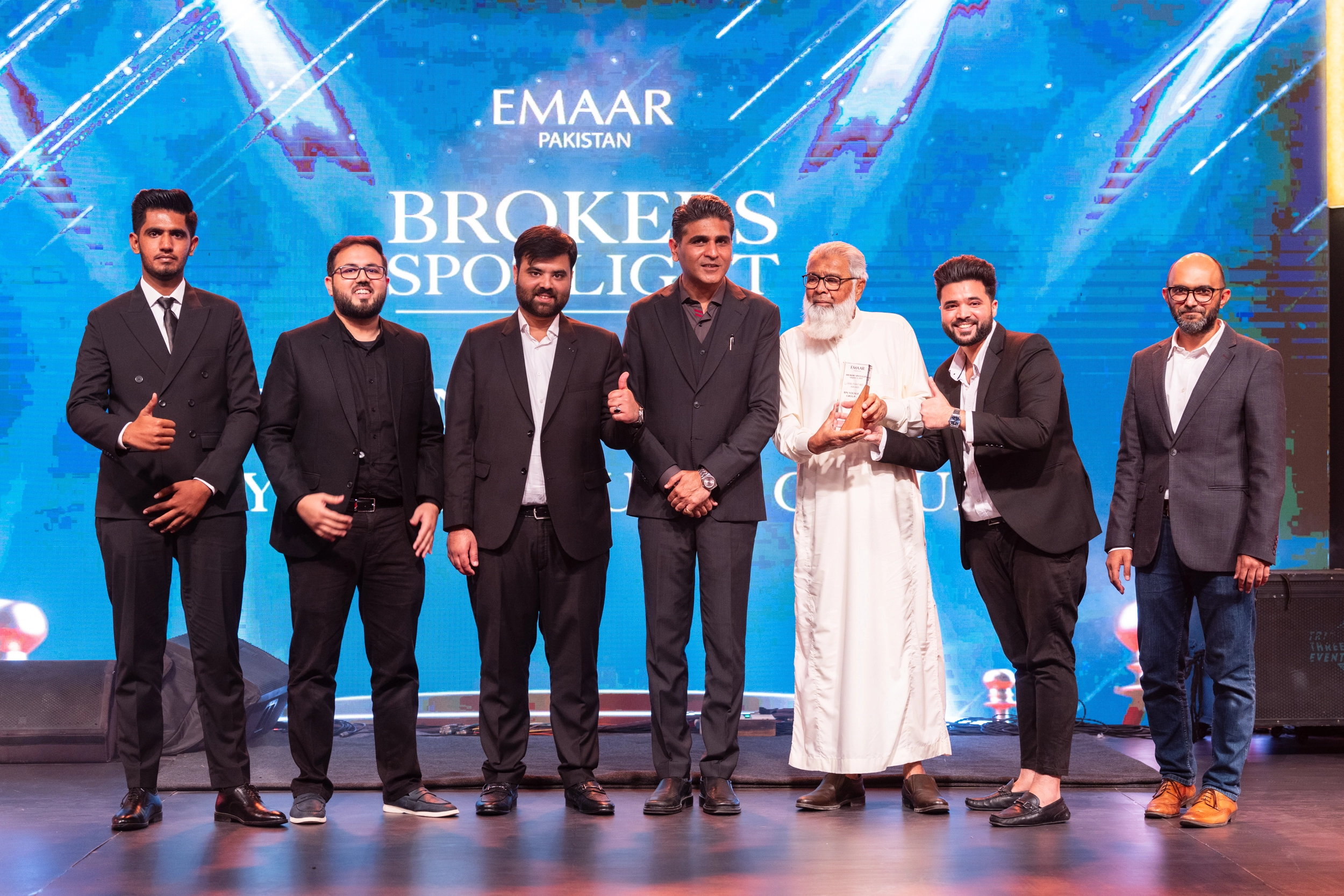 BinYousuf Group team of seven members standing on stage at Emaar Pakistan Brokers Spotlight Award ceremony, holding award trophy, with branded backdrop